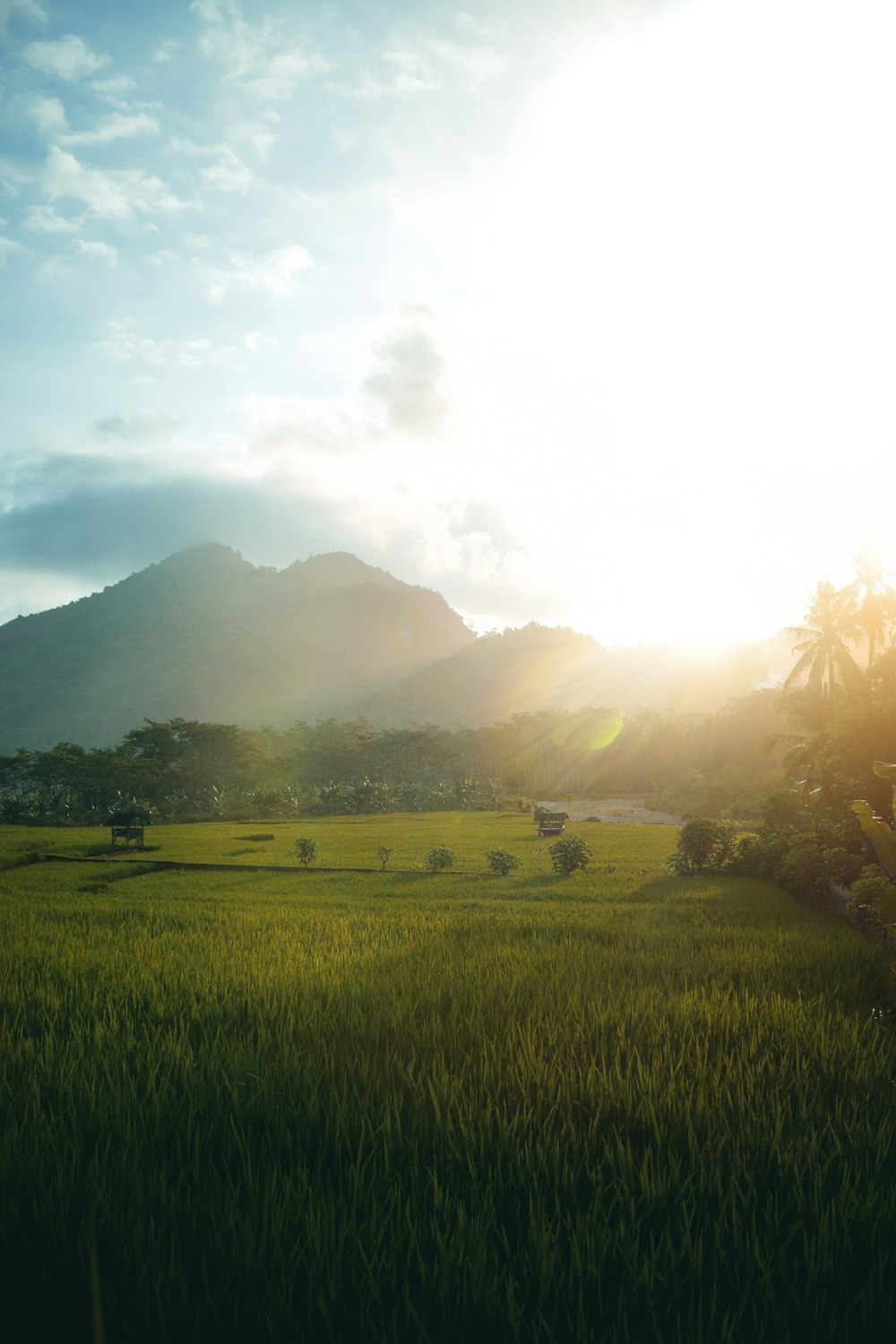 green grass field near mountain under white clouds during daytime