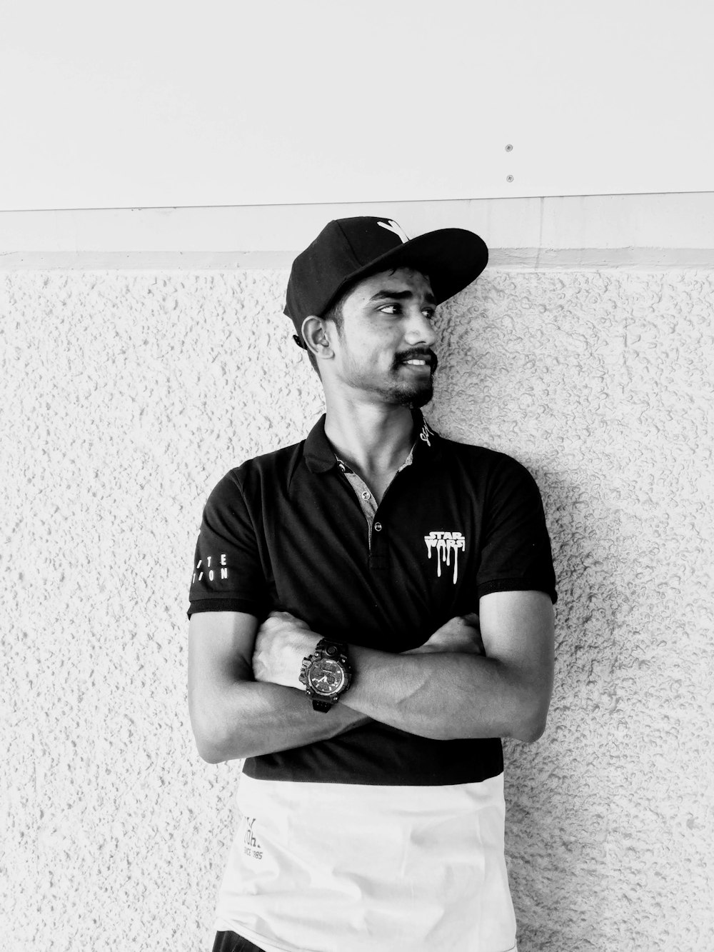 man in black polo shirt and black hat leaning on wall