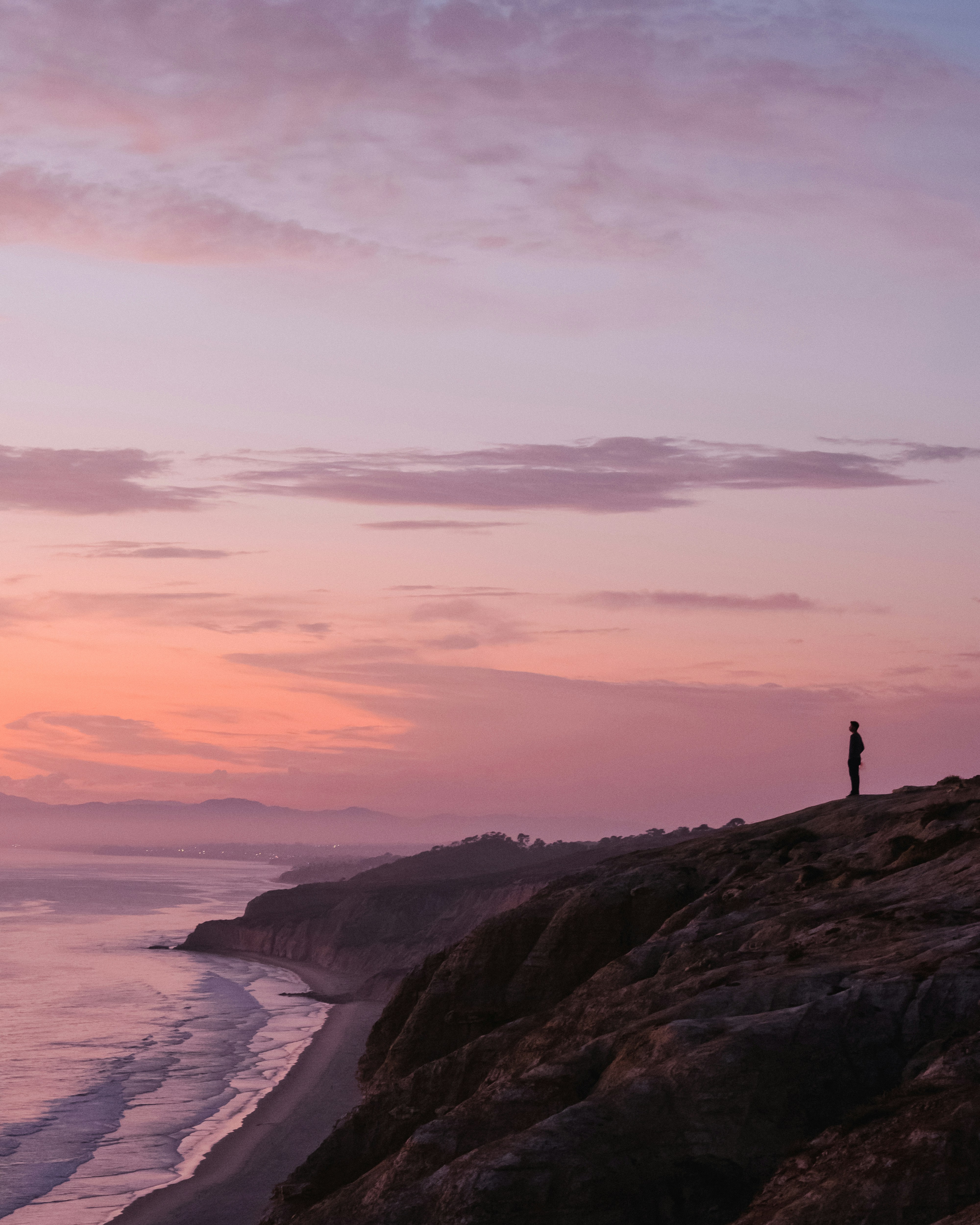 silhouette of person standing on rock formation near body of water during sunset
