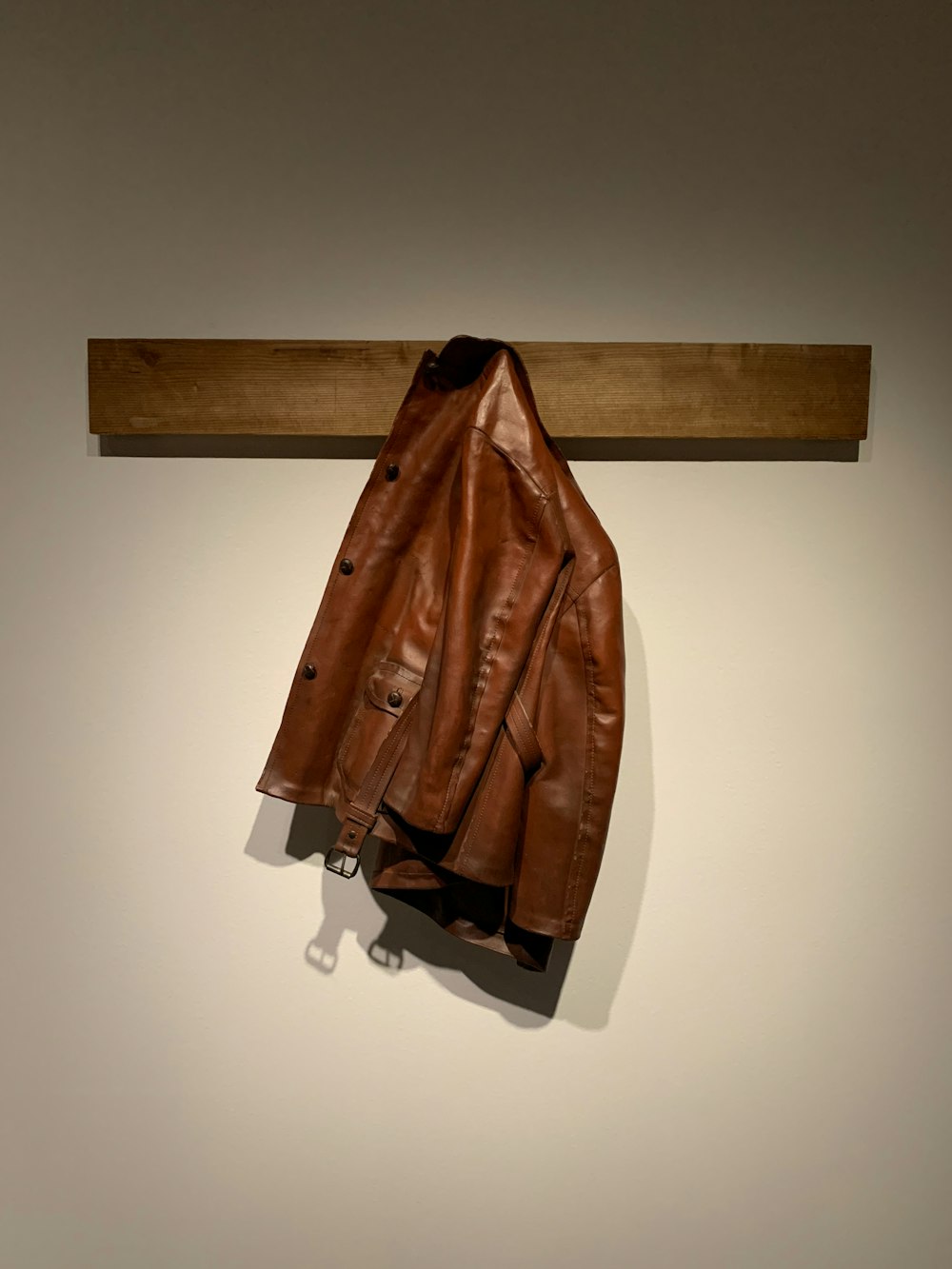 brown leather jacket hanging on brown wooden wall hook