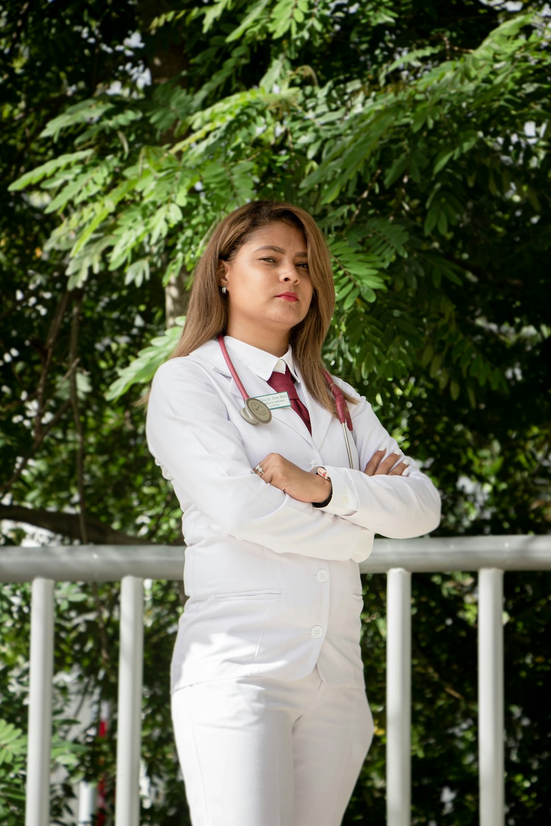 woman in white dress shirt and white pants standing near green tree during daytime