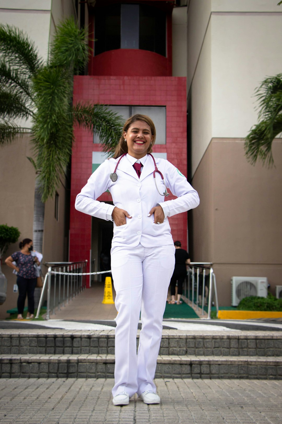 woman in white dress shirt and green pants standing near red building during daytime