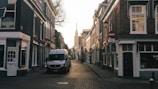 A wide shot of the van parked beside a quiet European village street lined with stone houses.
