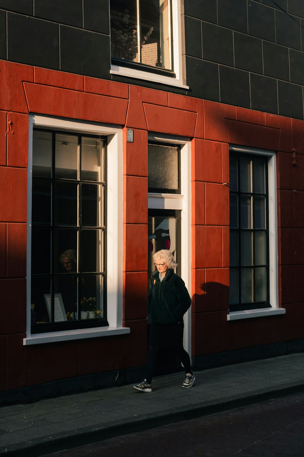 homme en veste noire debout devant un bâtiment en béton brun pendant la journée