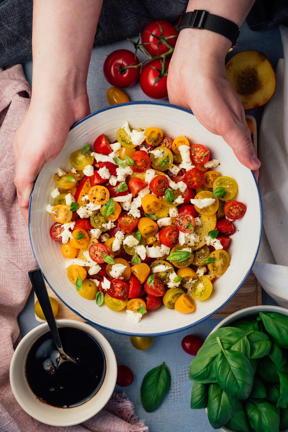 Persona sosteniendo un plato de ensalada de tomate en rodajas y verduras verdes