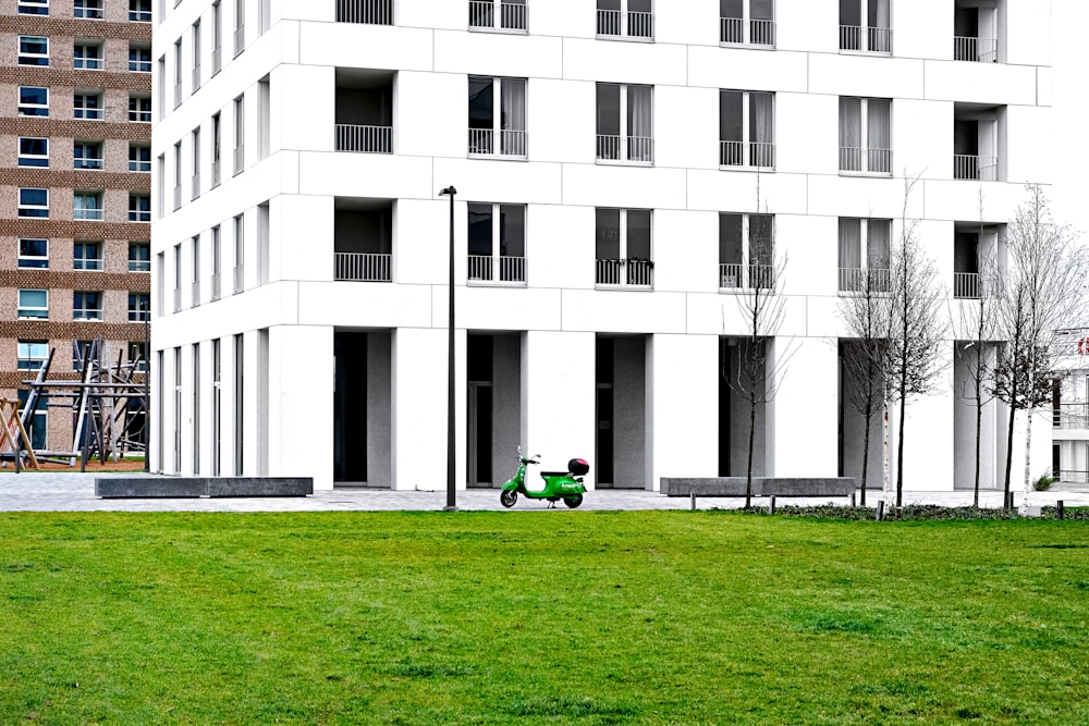 昼間、白いコンクリートの建物の近くの緑の芝生に座っている緑のシャツを着た人