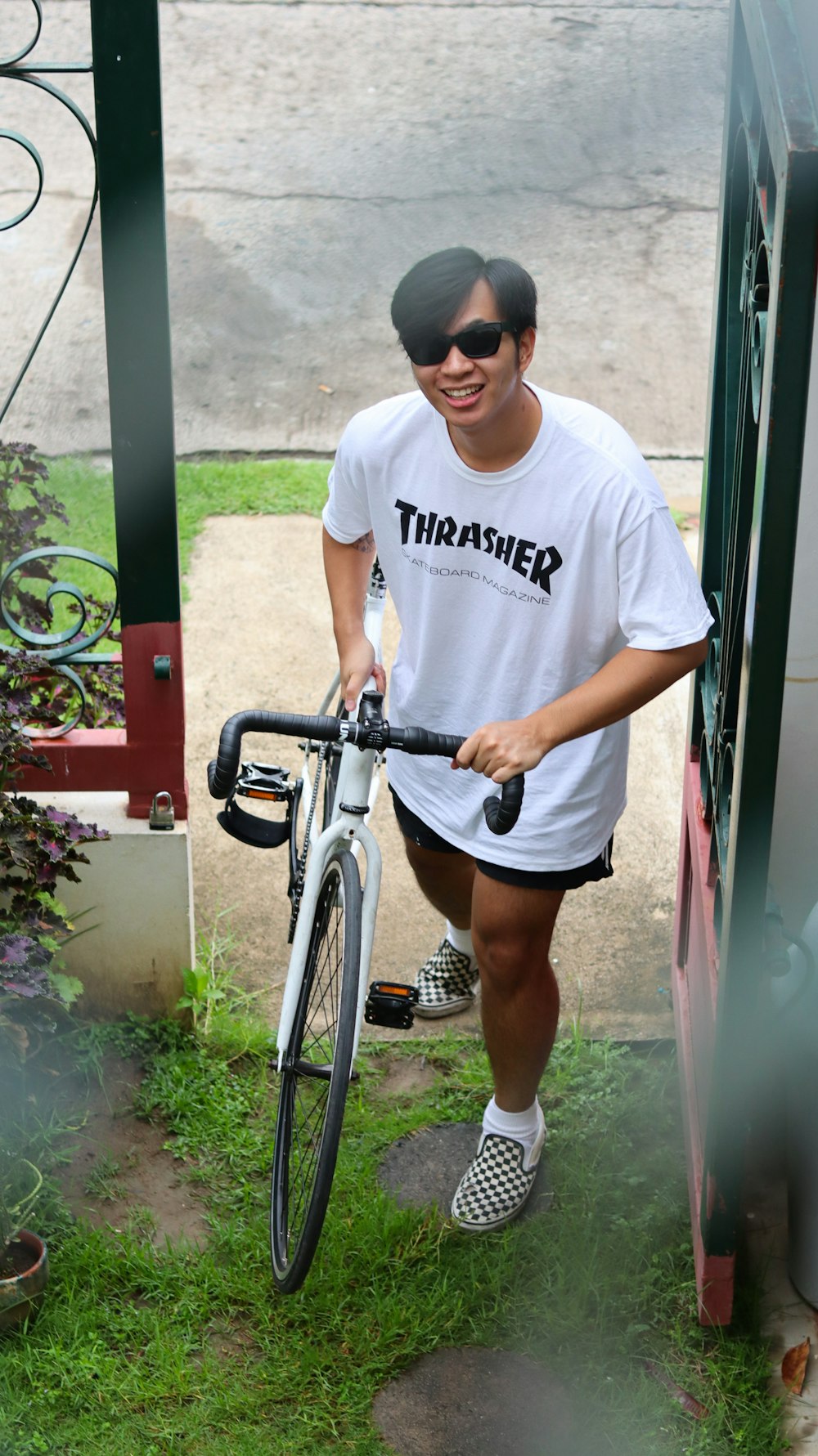 man in white crew neck t-shirt and black shorts standing beside black and gray bicycle