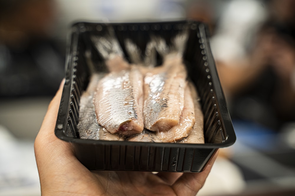 person holding black plastic tray with meat