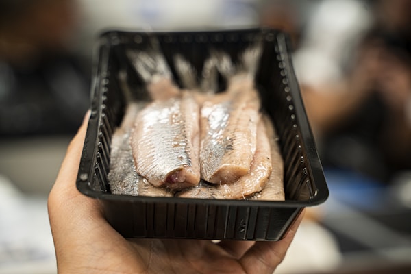 Person holding black plastic tray with meat