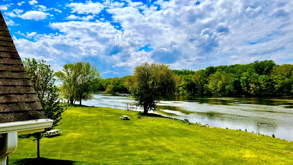 green grass field near lake under blue sky and white clouds during daytime