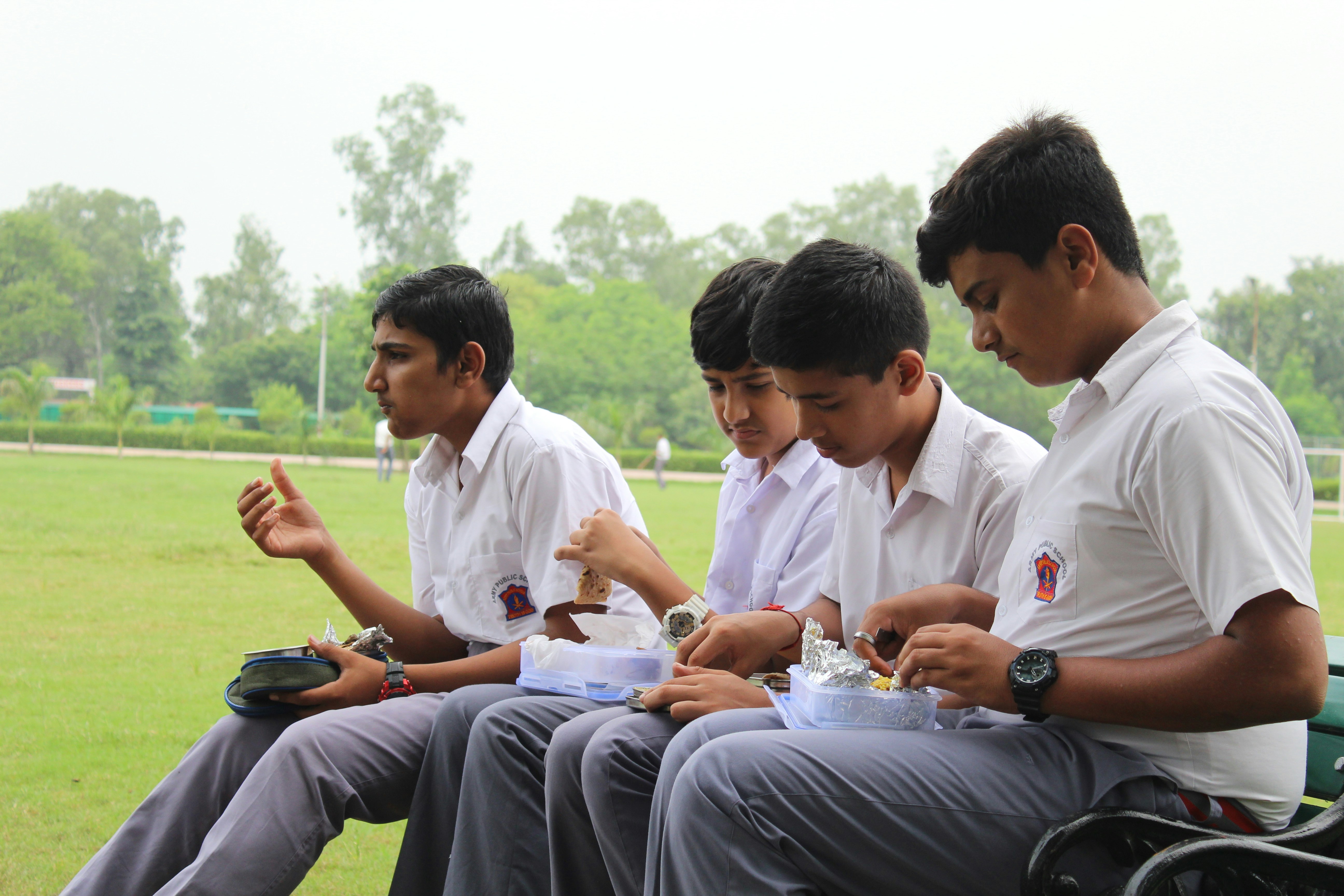 Four Indian primary school students having lunch in the playground on a bench during school break.<br /><br />School reopening after corona