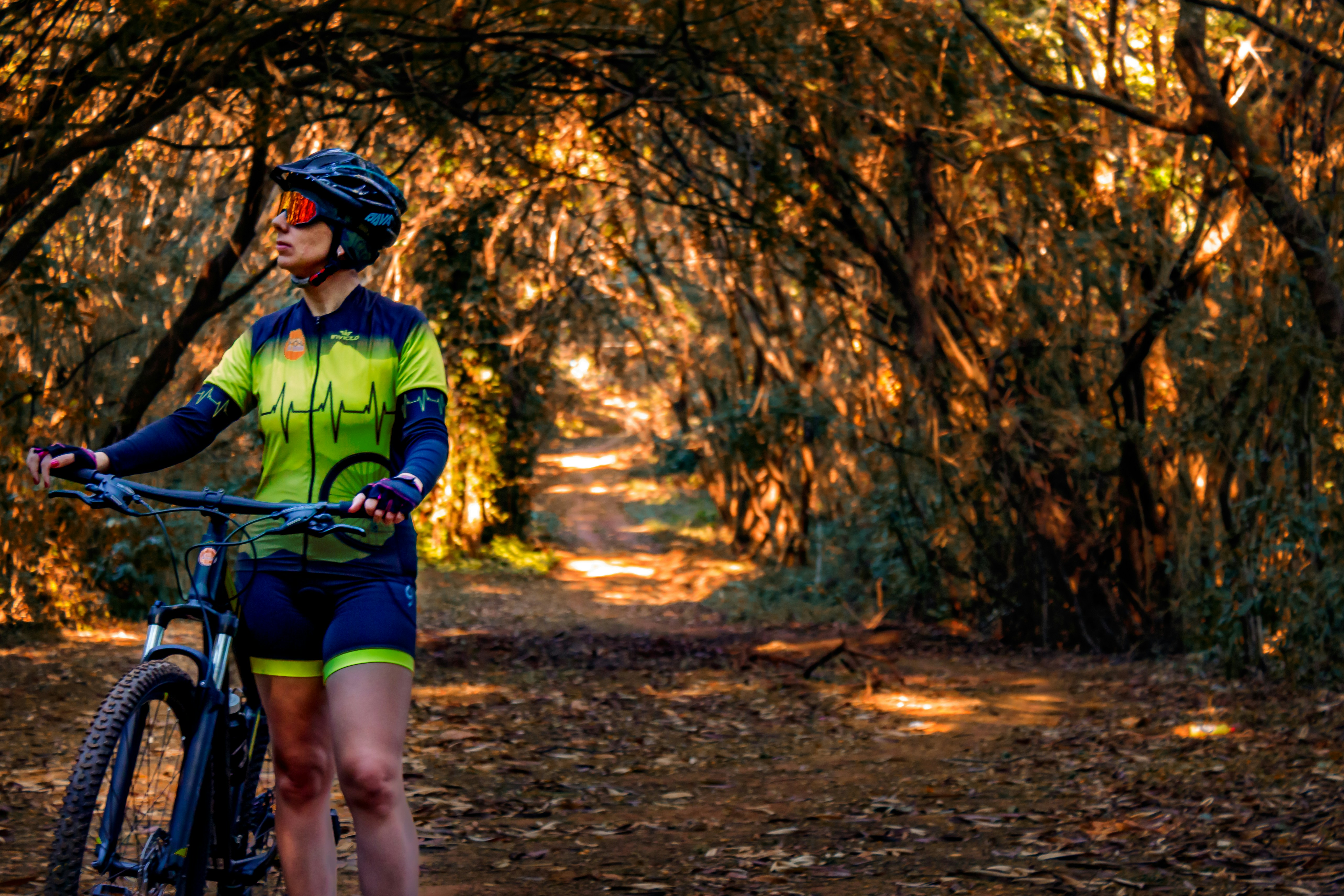 Cyclist reaching for a water bottle on a sun-drenched trail, bright outdoor daylight, vibrant green foliage background