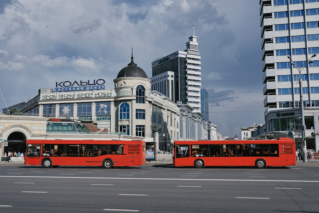 red double decker bus on road near city buildings under white clouds during daytime