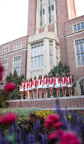 A group of young ladies in crimson and cream dresses smiling at the cotillion event.
