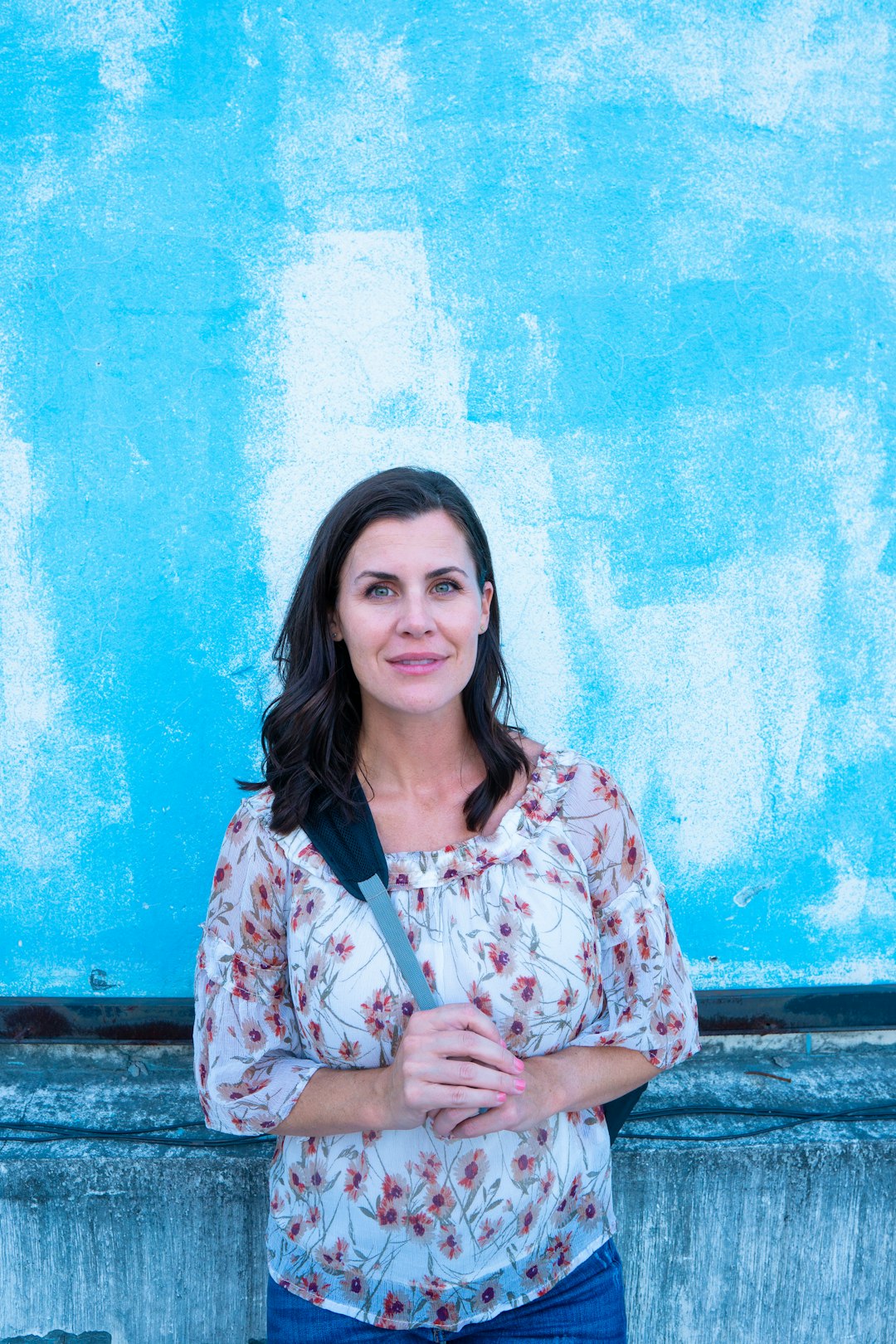 woman in white and red floral button up shirt standing beside blue wall