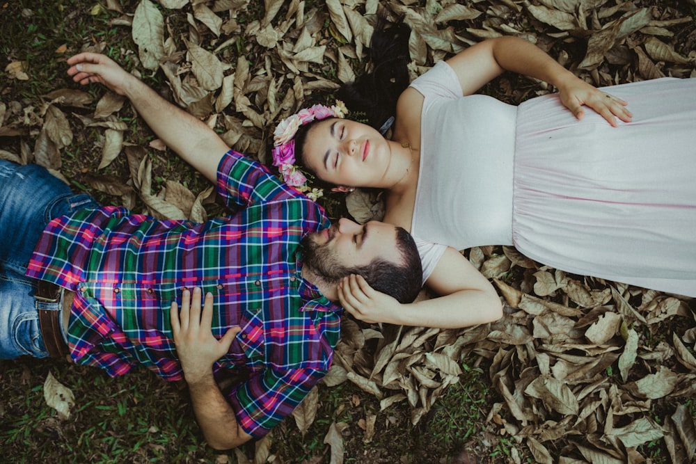 man in white tank top lying on ground beside woman in red and black plaid dress