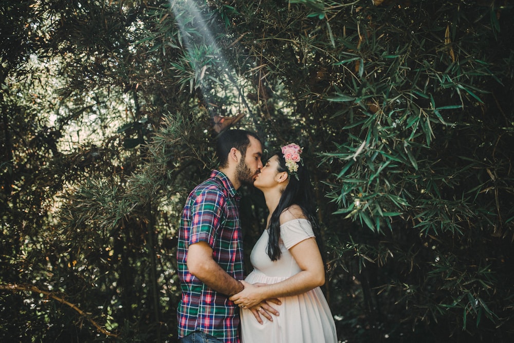 man and woman kissing under green tree during daytime