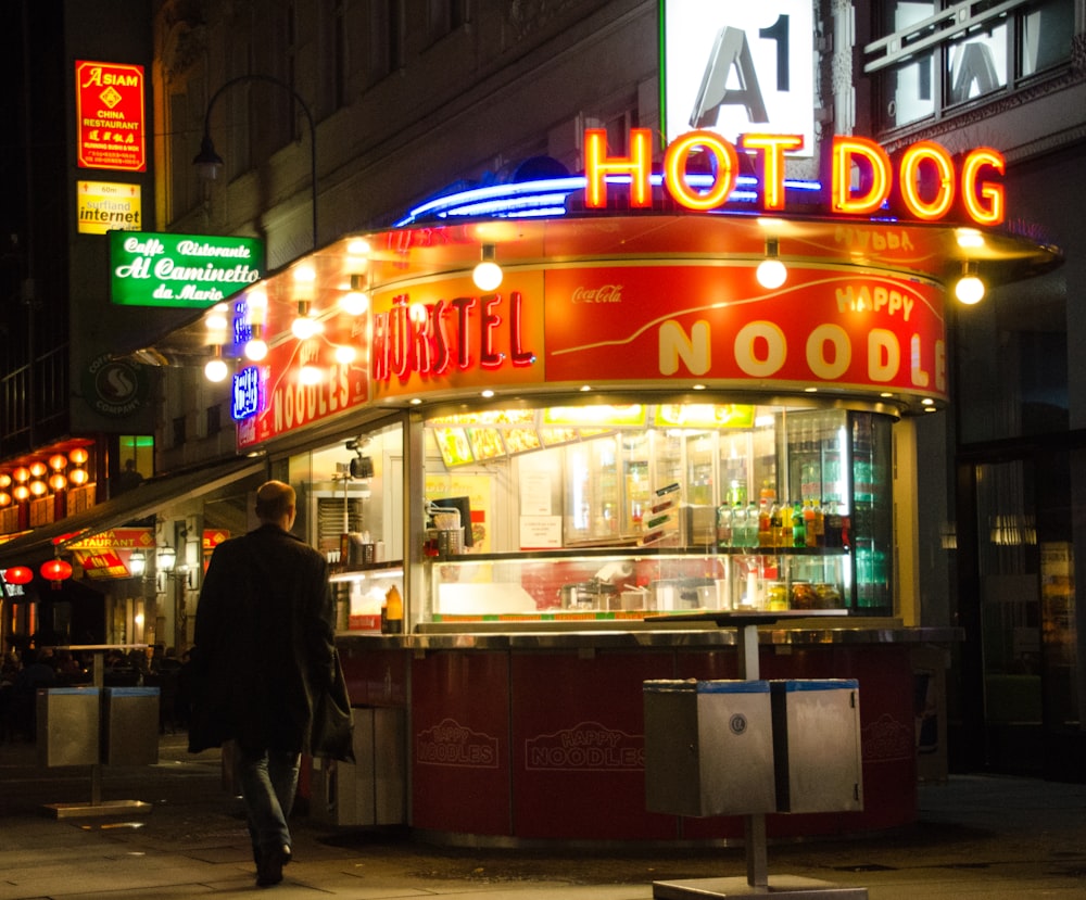 a man walking down the street in front of a hot dog stand