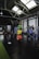 A spacious gym interior with high ceilings and large skylights providing natural light. Various gym equipment, including weight racks with colorful plates (green, yellow, red, blue), a pull-up rig, and exercise machines are neatly organized. The space has a mix of black flooring and a strip of green turf, creating a clean and organized workout environment.