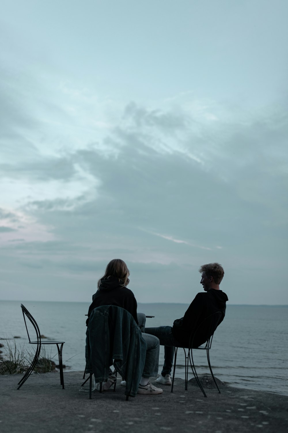 couple sitting on chair near body of water during daytime