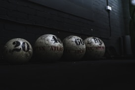The image depicts four large weighted balls arranged in a row against a dark background. Each ball is labeled with a number indicating its weight, such as 20, 40, 60, and another obscured number. The setting suggests a gym or fitness environment, characterized by dim lighting and a focus on the rugged texture of the equipment.