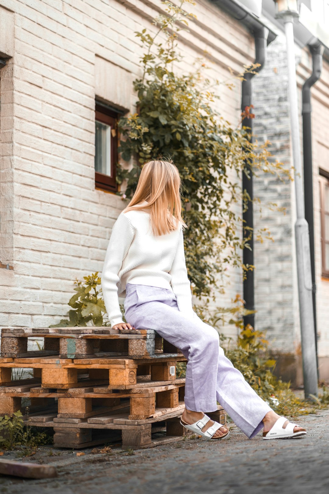 woman in white long sleeve shirt and white pants sitting on brown wooden crate