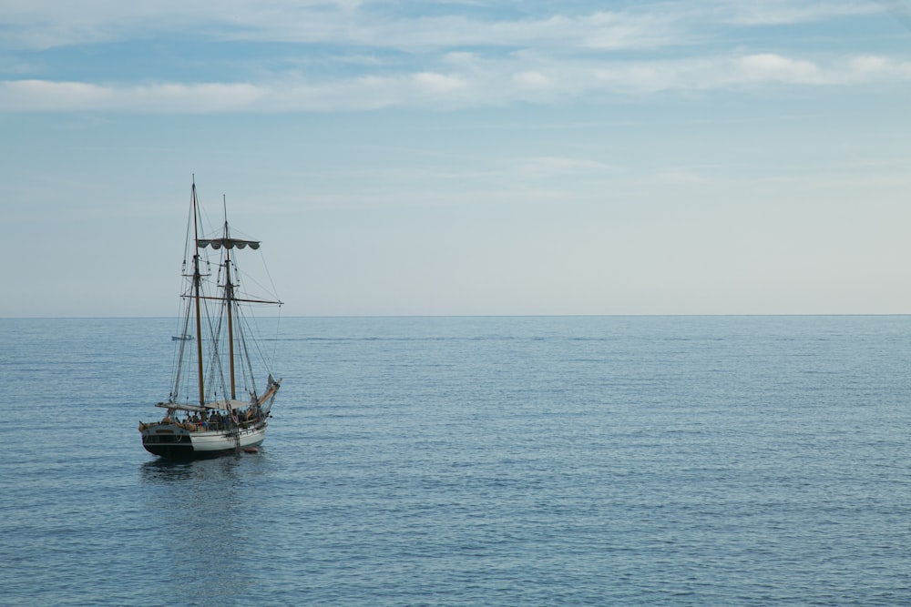 black sail boat on sea under white clouds during daytime