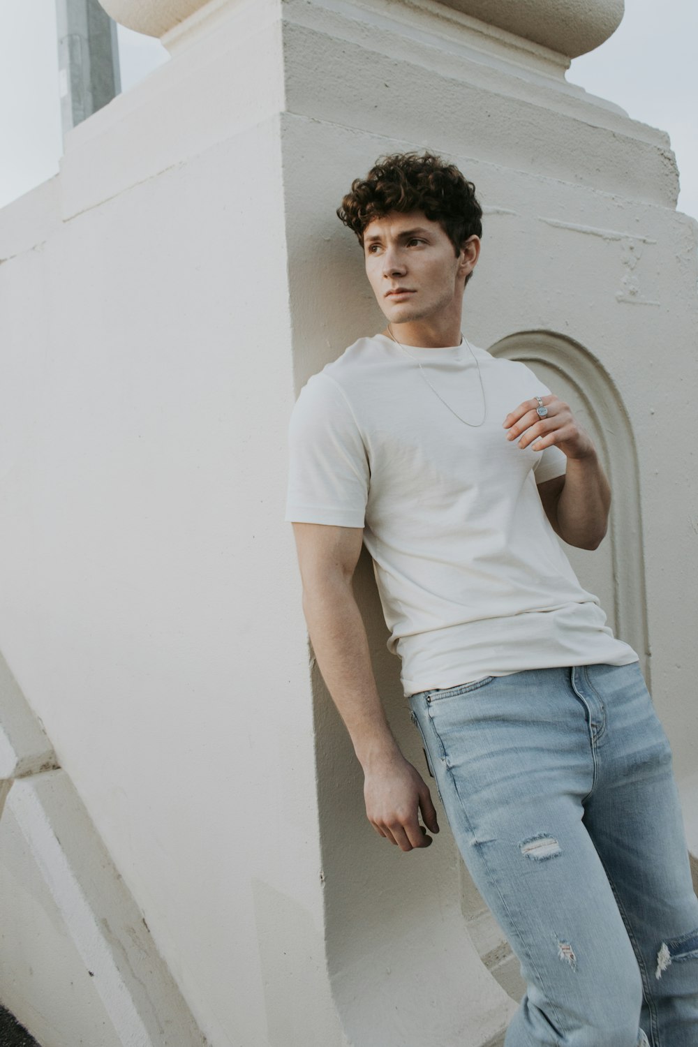 Hombre con camiseta blanca de cuello redondo y jeans de mezclilla azul de pie junto a la pared blanca