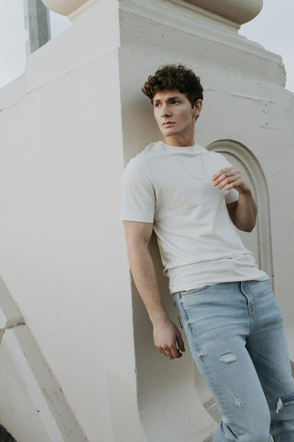 man in white crew neck t-shirt and blue denim jeans standing beside white wall