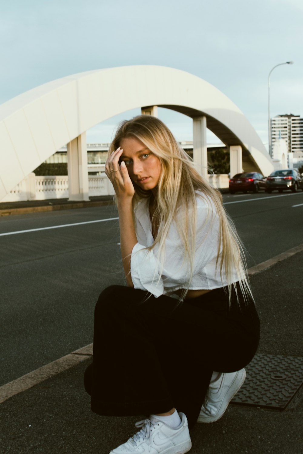 woman in white long sleeve shirt and black pants sitting on gray asphalt road during daytime