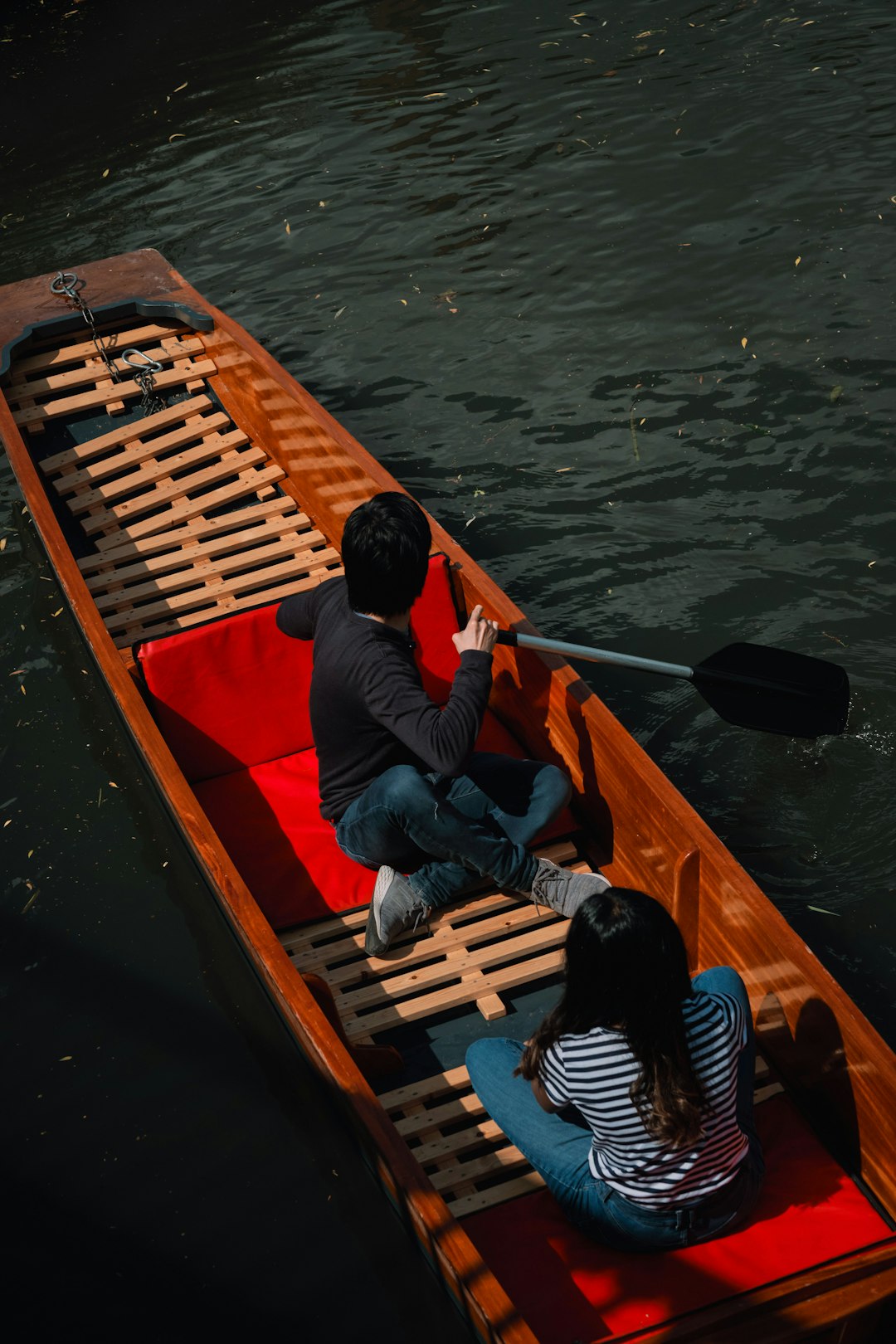 man in red shirt and blue denim jeans sitting on brown wooden boat