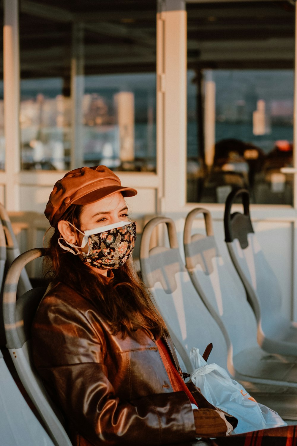 woman in brown leather jacket and brown knit cap sitting on white plastic chair