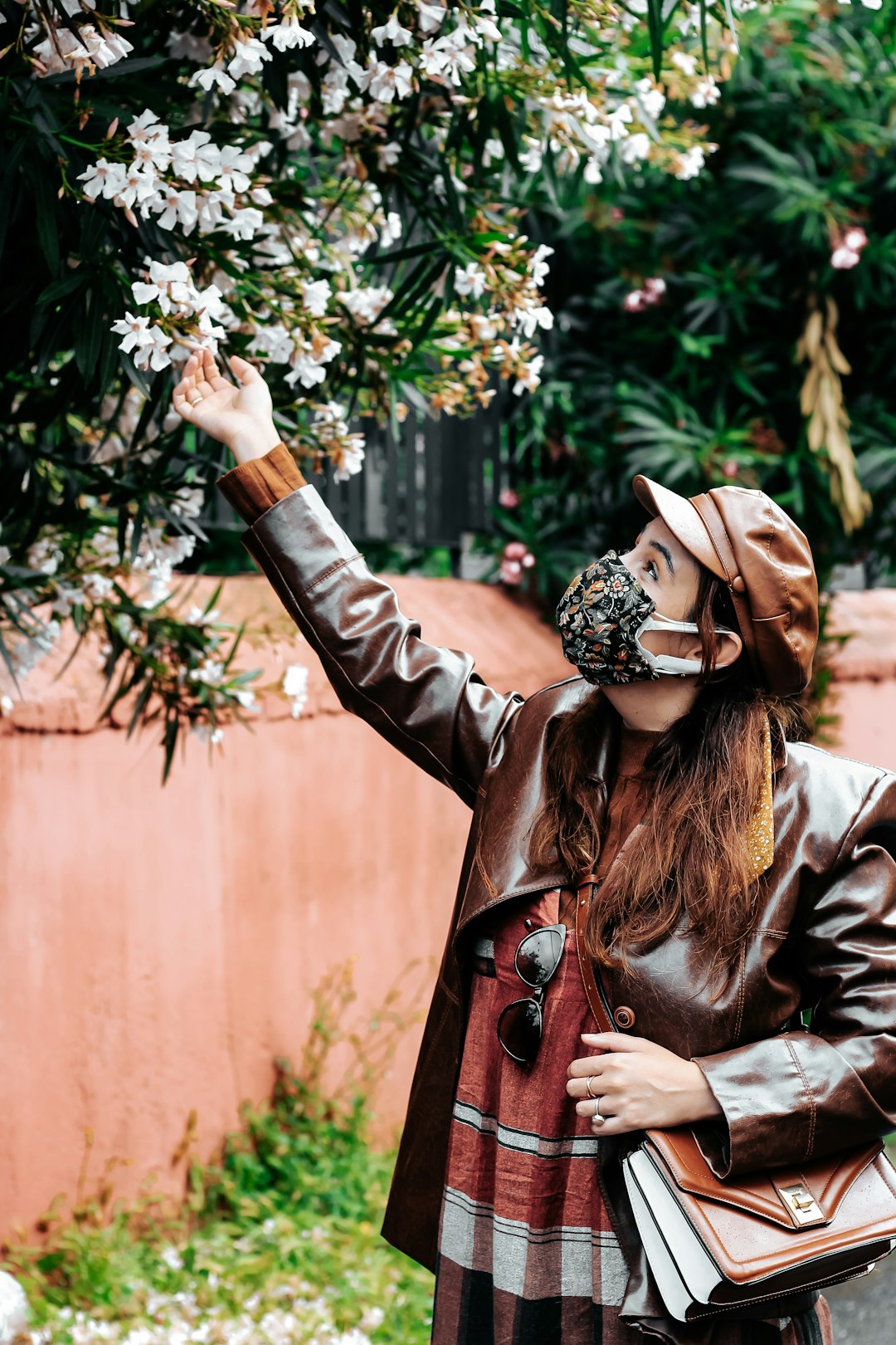 woman in brown leather jacket and white and black floral headdress standing beside brown wall