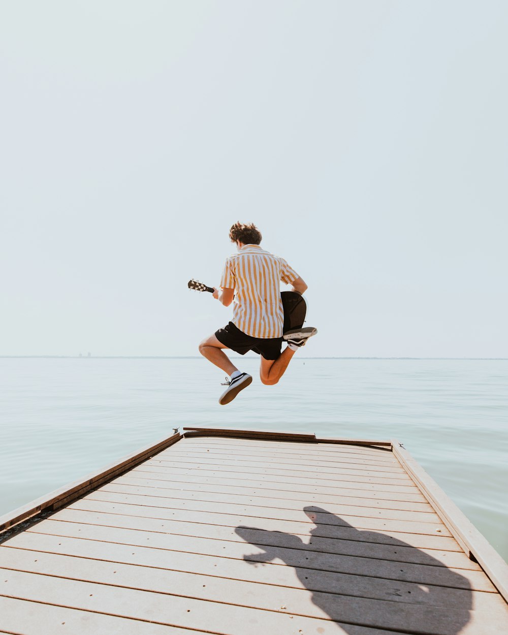 man in white and black stripe shirt and black shorts jumping on dock during daytime