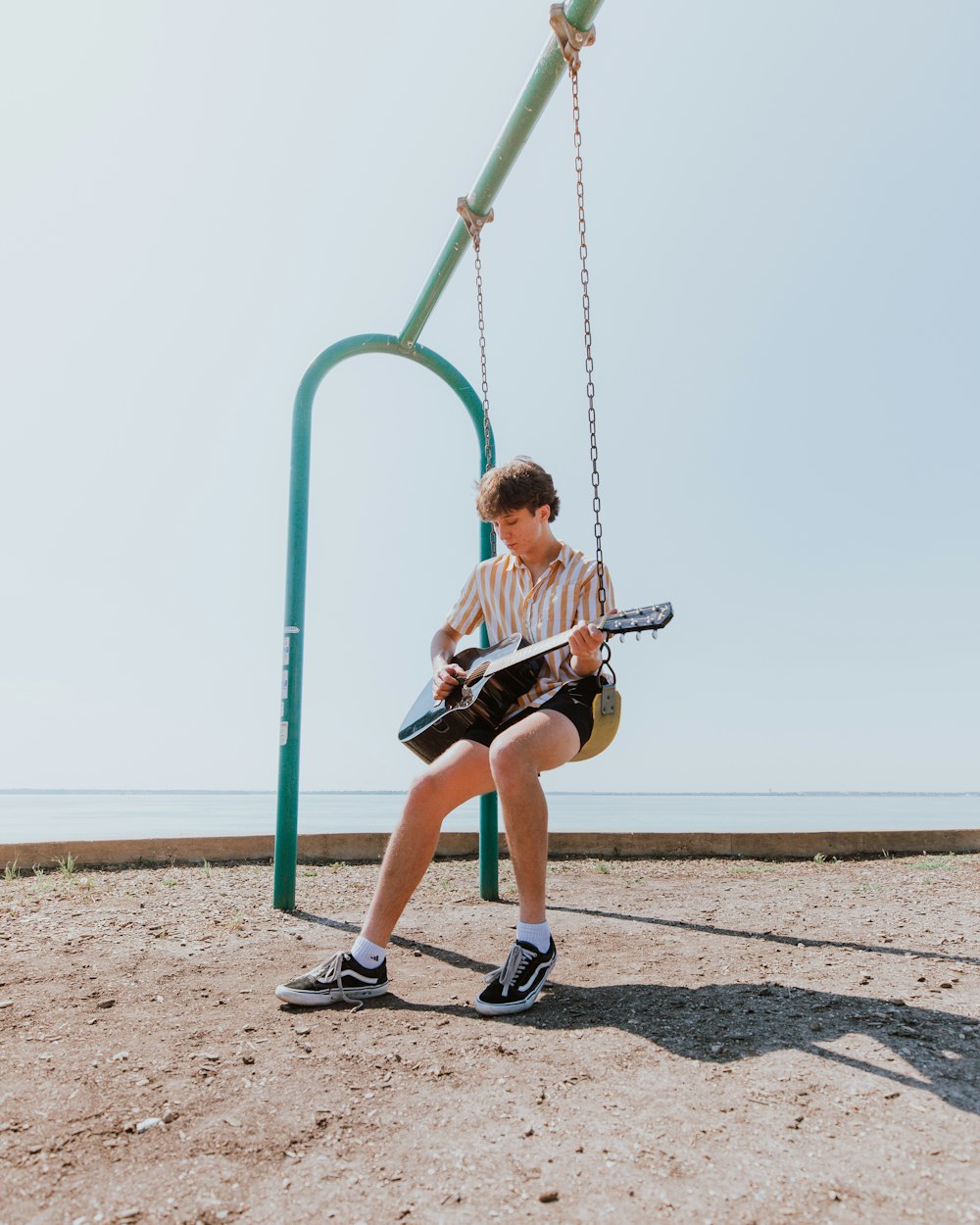 man in white t-shirt and red shorts sitting on green metal swing during daytime