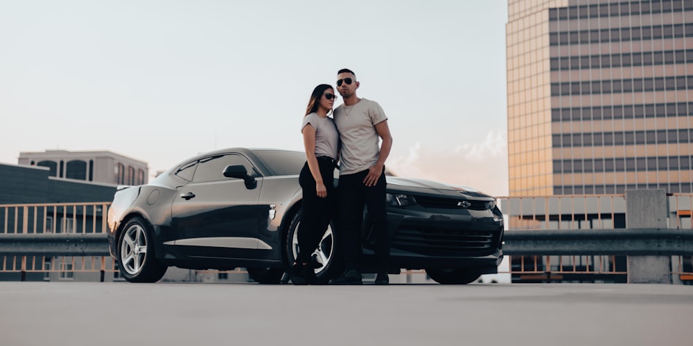 man in white t-shirt and black pants leaning on black car