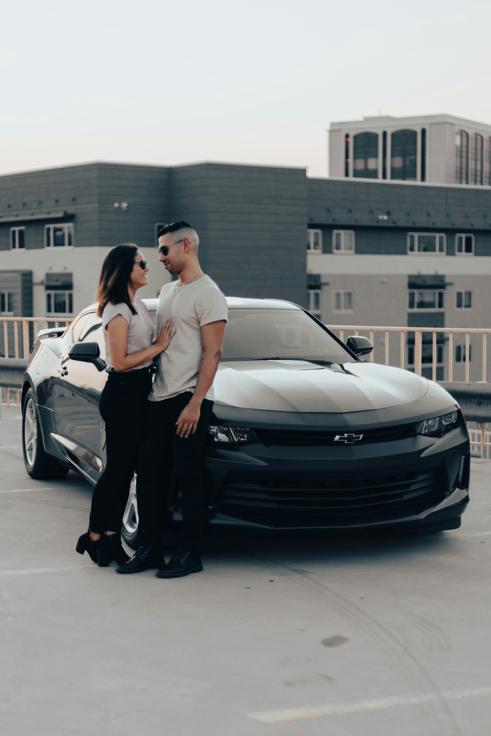 man in white t-shirt and black pants leaning on black car