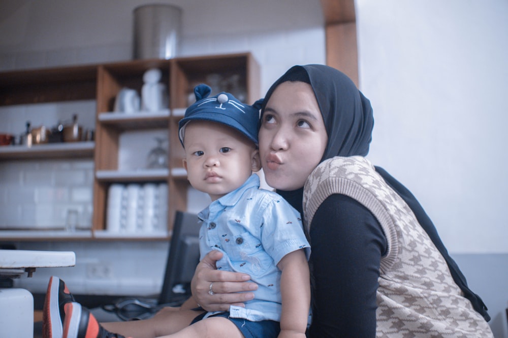 woman in black hijab carrying baby in blue onesie