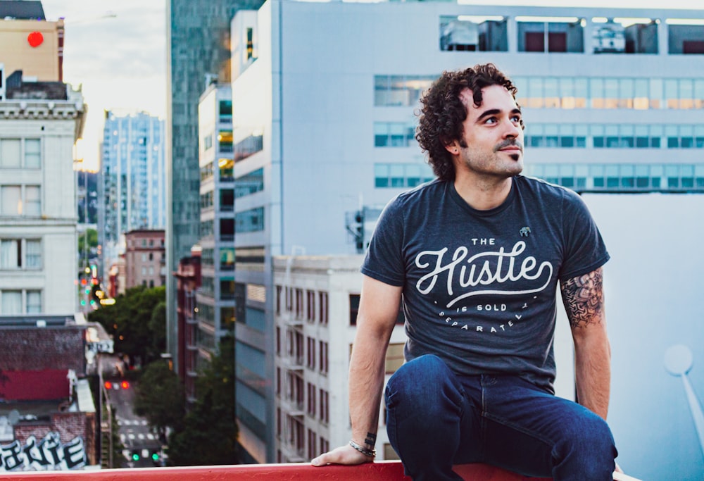 man in black crew neck t-shirt sitting on brown wooden bench during daytime