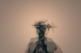 A double exposure photograph combines the silhouette of a person with a bouquet of flowers, creating a surreal and artistic effect. The person's outline is partially transparent, allowing the floral elements to stand out.