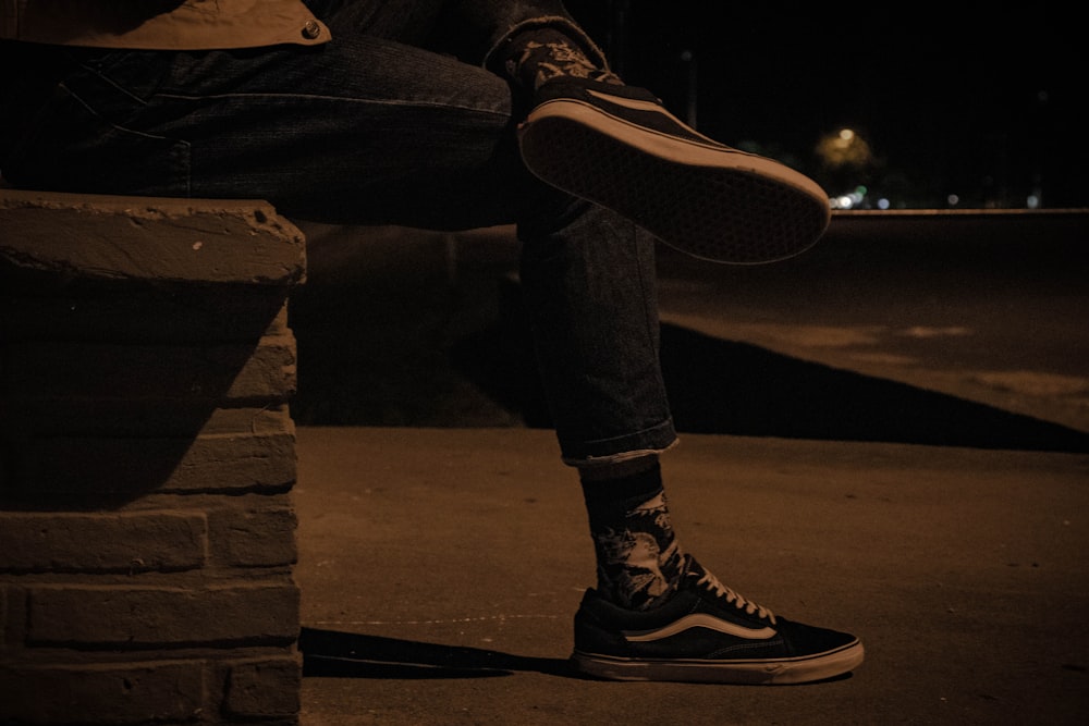 person in black pants and black sneakers sitting on concrete bench