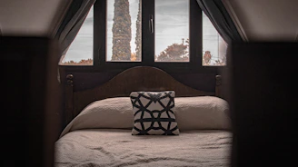 A bright bedroom featuring soft linens and a large window overlooking trees.