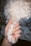 A hand with colorful, artistic nail art holds a fluffy white dog's paw. The nails feature intricate designs, such as stripes and swirls. The dog's fur is curly and white, and it contrasts with the painted nails.