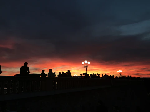 Volunteers handing out warm meals to people gathered under a city bridge at sunset.