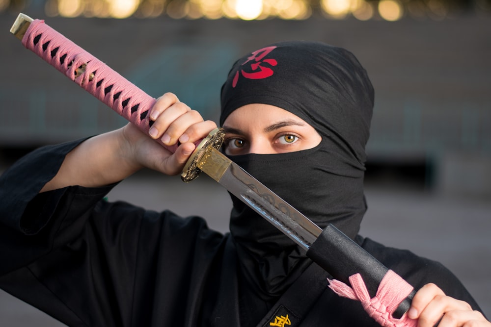 Femme en hijab noir tenant une épée rose et noire