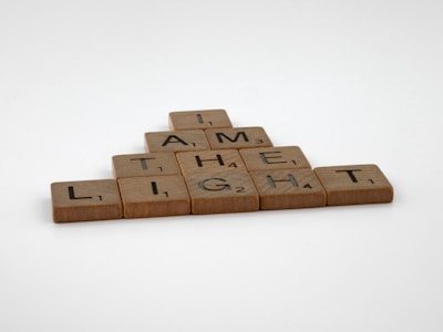 Wooden letter tiles are arranged to form the phrase 'I AM THE LIGHT' in a pyramid structure on a plain background.
