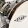 Close-up view of a drum with a wooden rim and chrome hardware. The surface is glossy with a textured pattern, and a logo is visible on the drumhead.