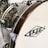 Close-up view of a drum with a wooden rim and chrome hardware. The surface is glossy with a textured pattern, and a logo is visible on the drumhead.