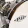 Close-up view of a drum with a wooden rim and chrome hardware. The surface is glossy with a textured pattern, and a logo is visible on the drumhead.