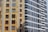 Tall residential buildings with multiple windows and balconies, showcasing architectural differences in colors and styles. One building has a yellow and beige facade with brown window frames, while the other is gray with white accents and modern design.